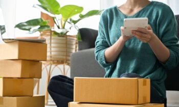 An online reseller holding a tablet and packing boxes while sitting on the living room floor for blog post on sourcing items