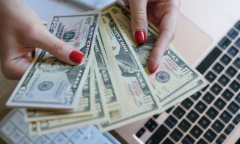 Closeup image of a woman's hands counting cash while using a laptop for blog post sign up and get free money