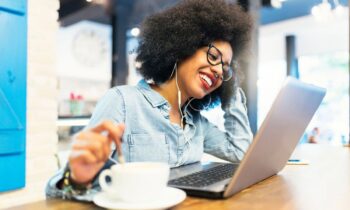 A woman working remotely from a cafe, using a laptop and drinking coffee for fun work from home jobs blog post