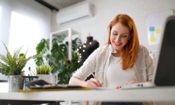 A woman sitting at a desk in her home office, using a computer to apply for remote jobs online.