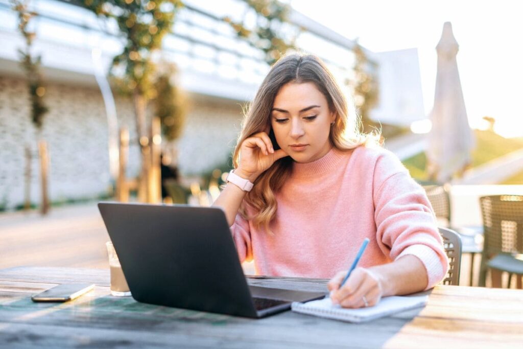 A woman working remotely from a cafe on a laptop outside.