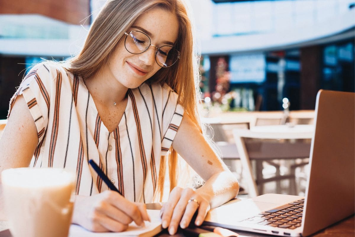 A woman working remotely from a cafe on a laptop outside.