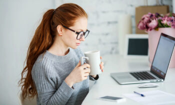 A female with long red hair and glasses proofreading documents from home