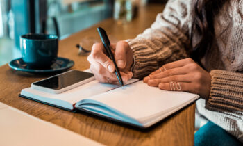 A female writing in a notebook listing the steps to break into freelance writing