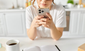 A middle aged female in her kitchen taking surveys using Survey Junkie on her phone