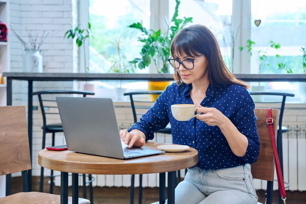 A middle aged woman drinking coffee and reading an article on her laptop titled top careers for people over 50