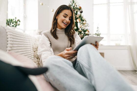 A middle aged woman sitting on the sofa looking at her iPad reading an article on ways to make Christmas cash