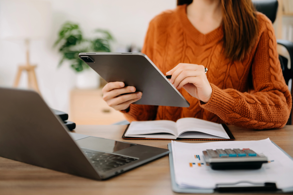 A woman wearing a sweater working on her tablet in her home office for her remote banking job