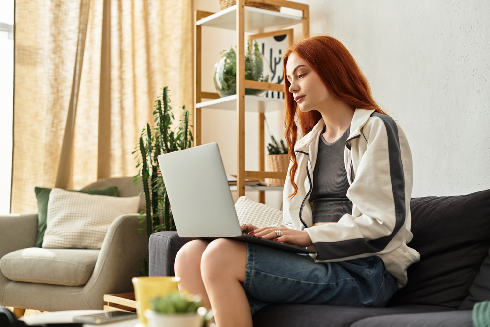 A woman with red hair sitting on her sofa looking for remote facebook jobs on her laptop