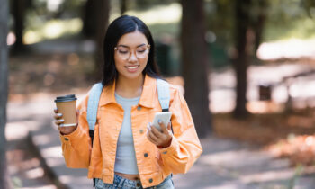 A young female drinking a coffee reading an article on her phone on hoe to get free stuff