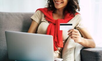 A woman sitting at home on a coach, using a laptop and holding a free Target giftcard.