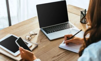 A woman working remotely from her home office, using a laptop and writing in a notebook for blog post how to write a follow-up email