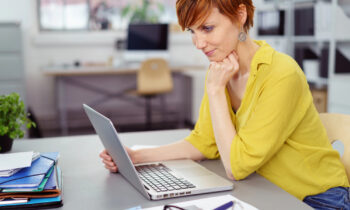 Middle aged woman with short hair reading an article on her latop titled 99 work at home career ideas for women