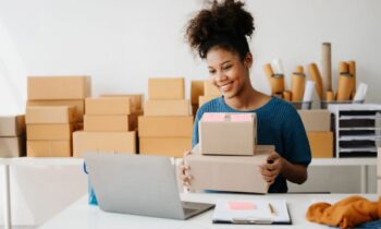 An online reseller using a laptop and packaging items for sale in a home office.