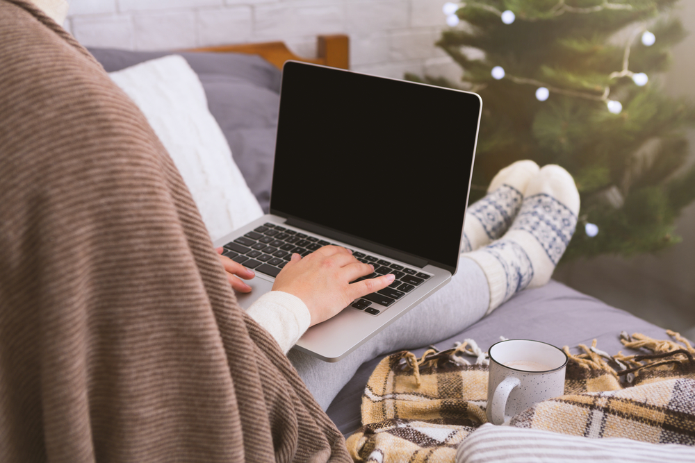 woman working on her laptop on the sofa in a sweater in front of a Christmas tree