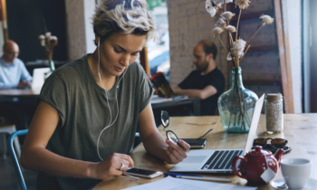 Young woman in a cafe looking for work from home jobs that provide equipment on her smartphone